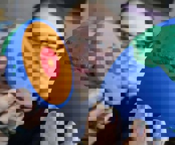 A female student holding a foam globe that has split into two to show what the inside of the earth looks like. The globe shows coloured layers to identify the core of the Earth.