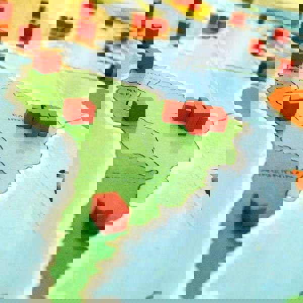 A close up of a board game on a table, depicting small red cubes on a map of South America