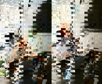 Two professionals having a conversation in an office with laptops in front of them