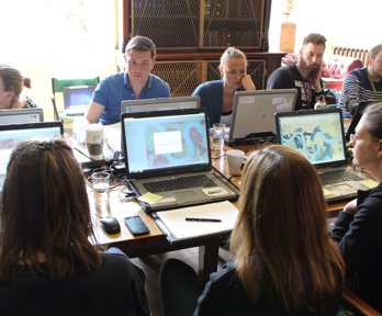 People sat around a table working on laptops with mapping software open.
