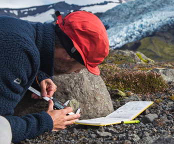 Person measuring the size of a mark on the side of a rock in a rocky landscape.