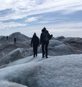 Four people walking across an undulating glacial landscape carrying equipment.