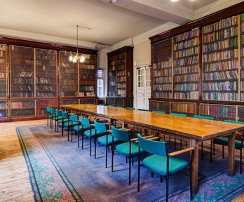 A grand historical meeting room with a long wooden table and bookcases.