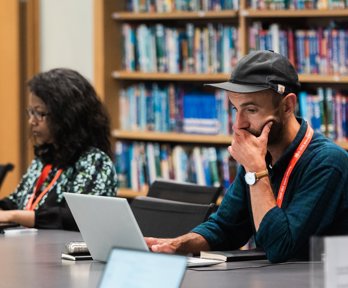 Two people using laptops while seated at a table in a library.