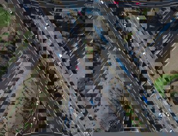 An aerial view of a motorway junction showing the roads crossing each other in an attractive pattern. Some roads are straight, others are curved. Each has multi coloured cars on it.