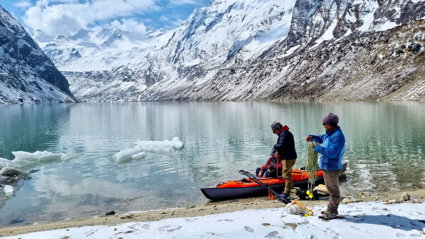 Two researchers on a lakeshore loading submersible temperature sensor arrays into a kayak, with snowclad Nepalese mountains in the background.