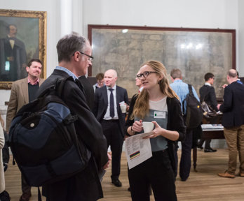 People scattered around and mid conversation in the Society's Map Room. Maps and portraits fill the walls behind.