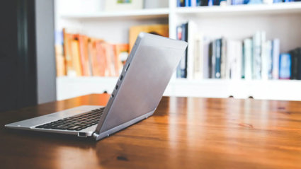 Open laptop on a table in front of a bookcase.