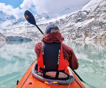 A kayaker approaches a glacier front in a Nepalese mountain landscape.
