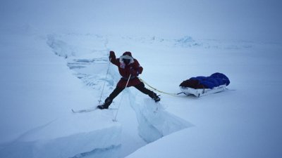 Person stretching between ice sheets in North Pole while attached to sled.