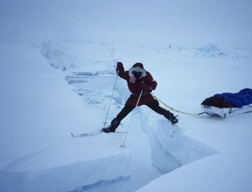 Person stretching between ice sheets in North Pole while attached to sled.