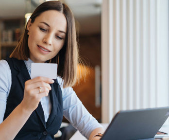 Person looking at a business card whilst sitting at a desk with a laptop.