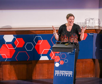 Speaker smiling while giving a lecture behind a lectern that says RGS expedition and fieldwork festival.