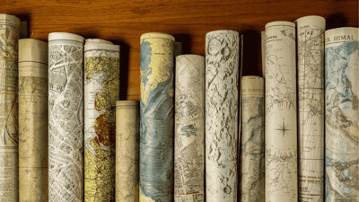 Rolled vintage maps standing upright in a row on a wooden surface.