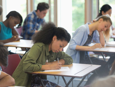 Students sitting at desks in a classroom, focused on writing during an exam.