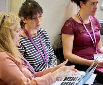 Three people sat with two people having a conversation while using a laptop.