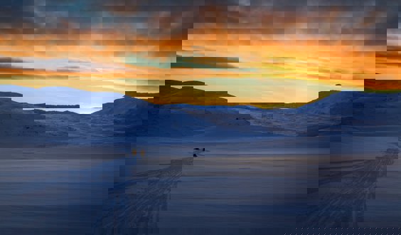 Snow capped mountain with people on snow mobiles and a sunset sky