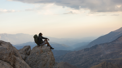 Backpacker sitting on a rock looking at the view of a mountain range.