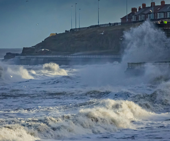 Waves crashing on shore near coastal residences.