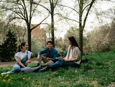 Three students sit in a park and chat.